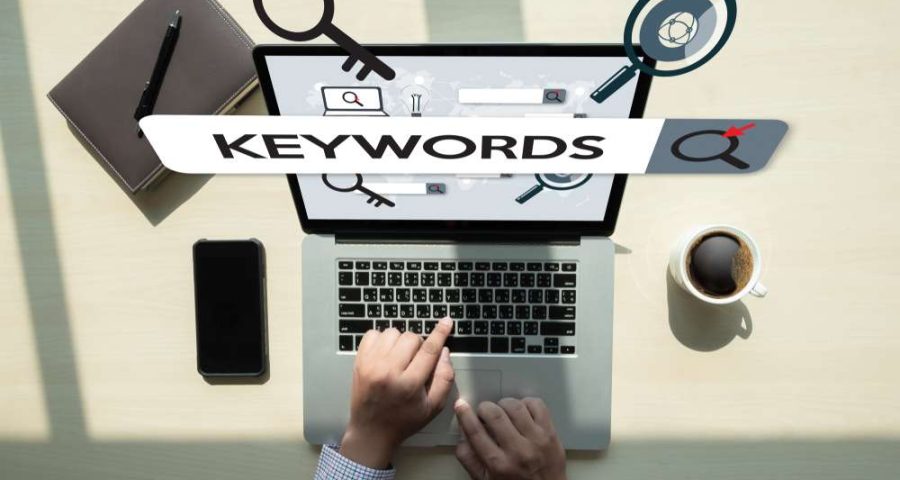 A person performing keyword research using a laptop with their phone next to them