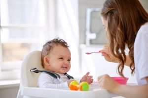 mother feeding happy baby in high chair a meal