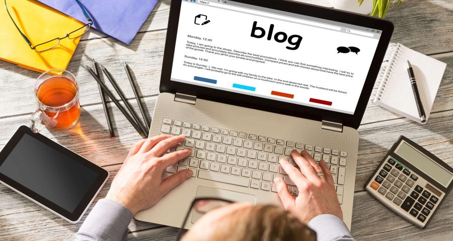 man typing on his laptop with a blog on the screen